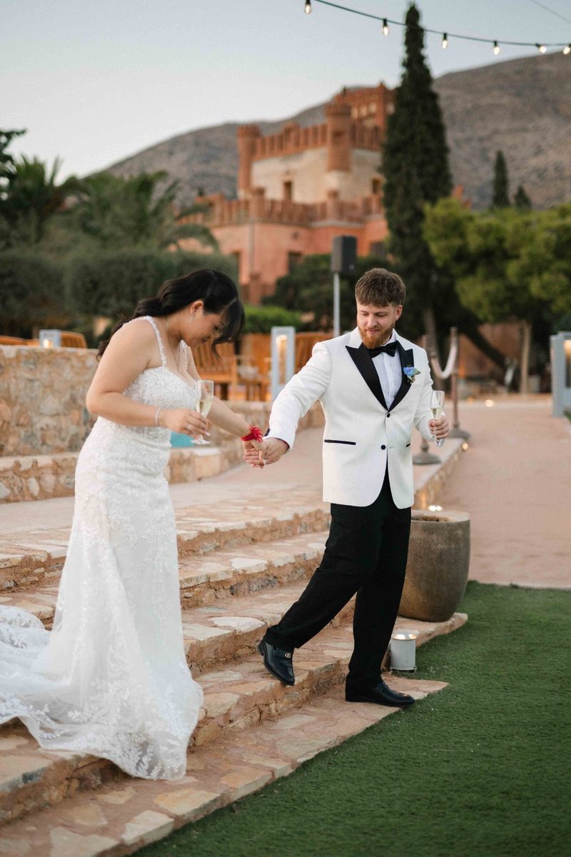 Couple descending stone steps at a Greek villa at golden hour — wedding photography by John Xenos, Greece.