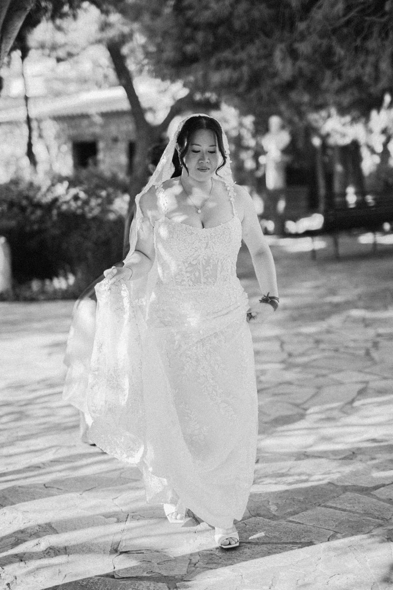 Bride walking alone on stone pavers in black and white — wedding photography by John Xenos, Greece.
